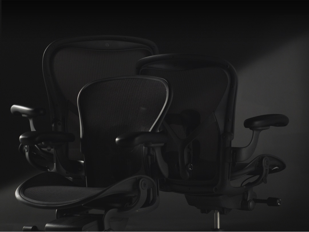 Three new Aeron chairs in Graphite finish are clustered together showing the difference in their sizes (one A, one B, and one C)