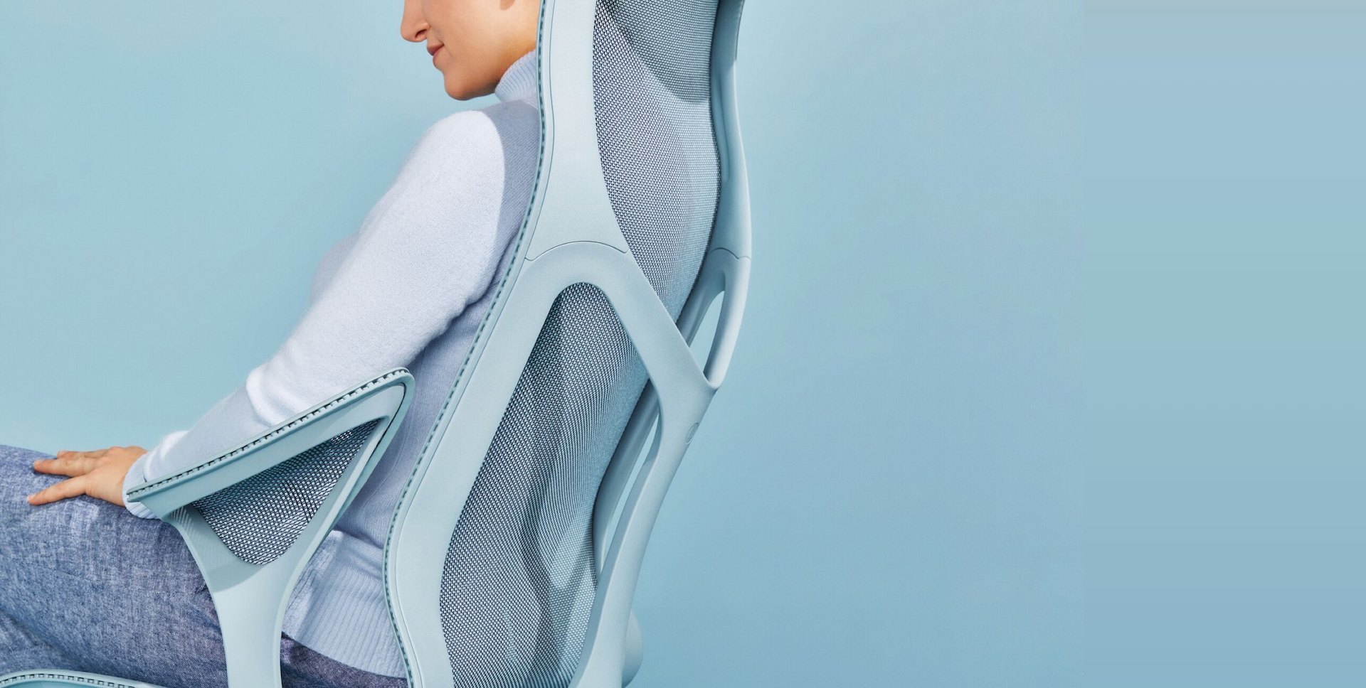 A woman wearing blue linen pants and a light blue sweater reclines in a Glacier light blue Cosm high-back ergonomic office chair.