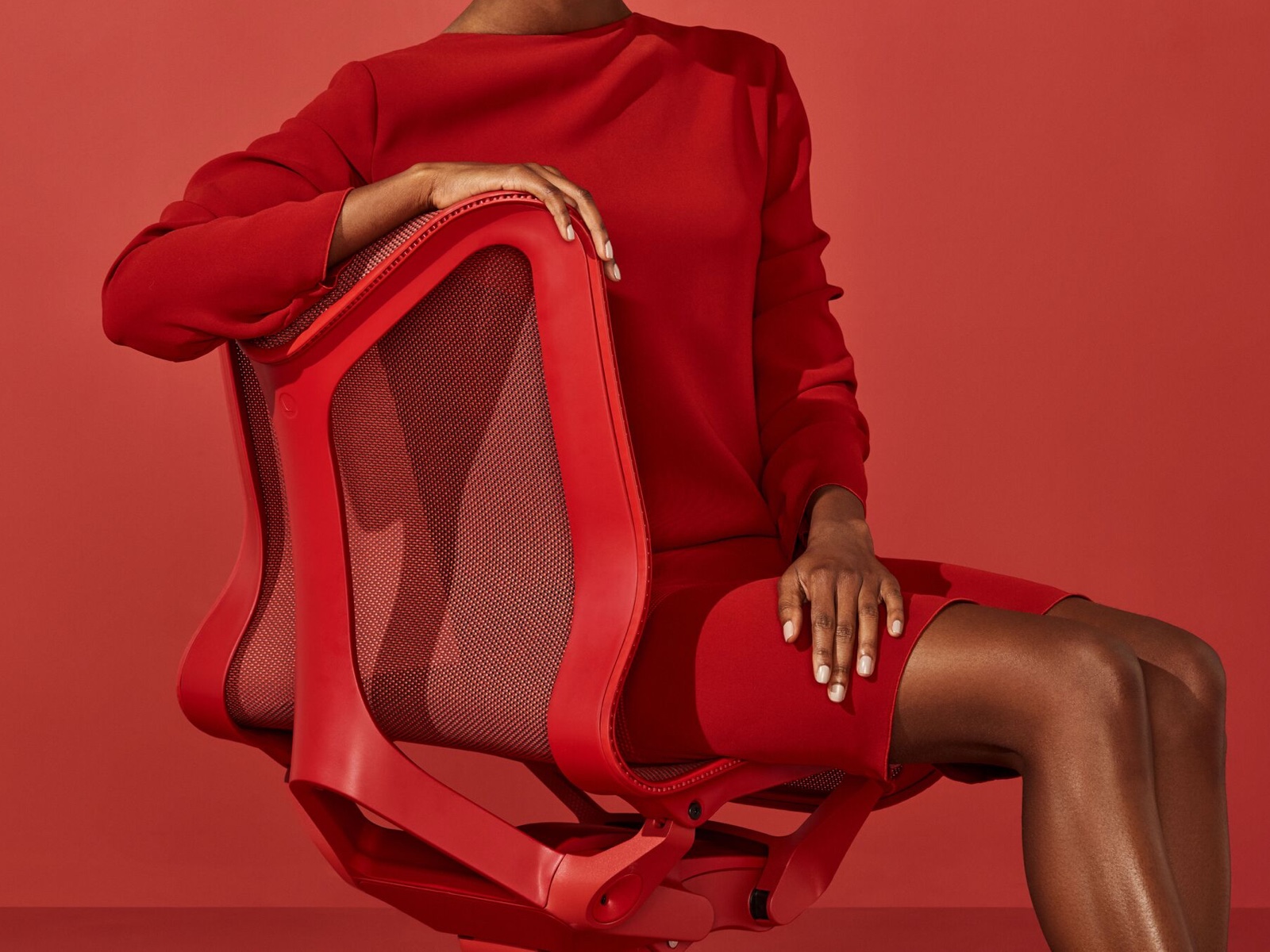 A woman in a red dress sits in a low-back Cosm Chair in Canyon red.