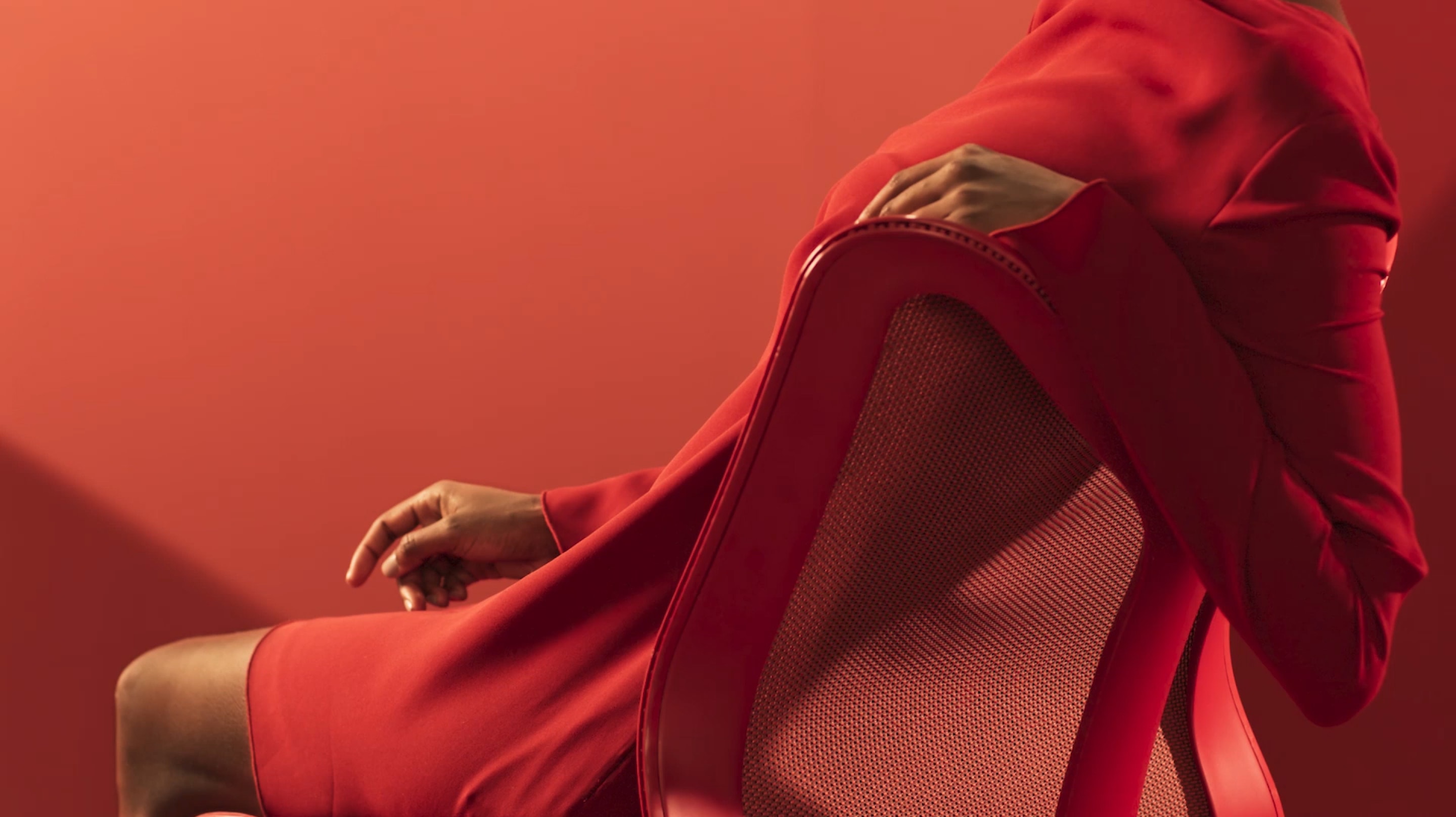 A woman in a red dress reclines with her arm over the backrest of a Canyon red Cosm Chair.